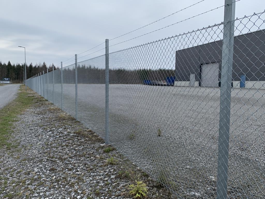 Flätverk med taggtråd – Förzinkat flätverksstängsel med taggtråd vid industrifastighet.